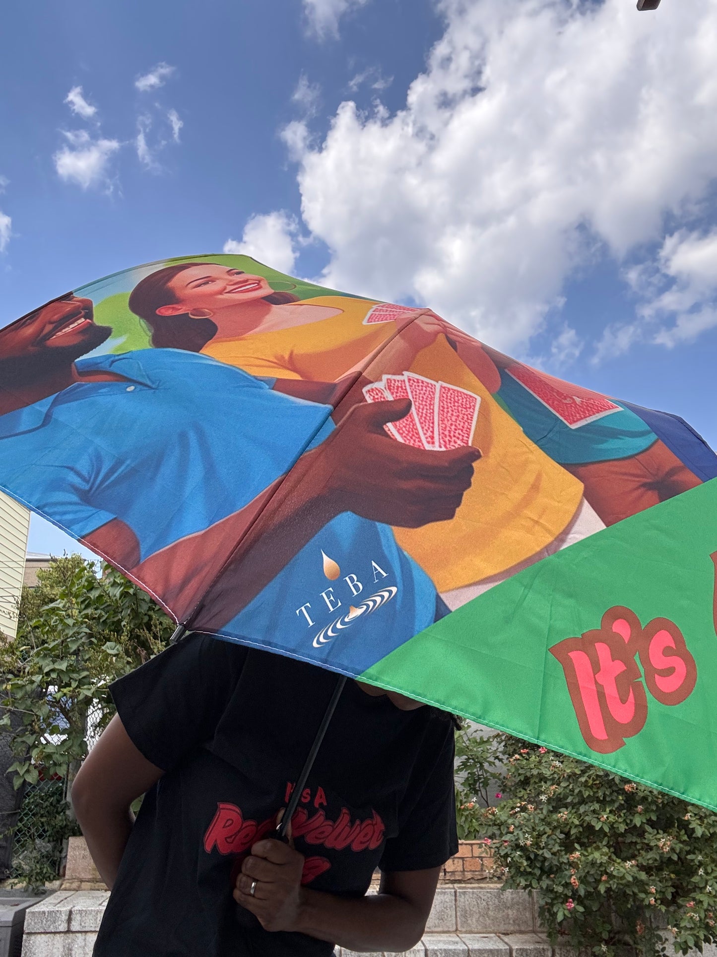 Colorful umbrella, with TEBA logo with artistic design held by a person against a blue sky.