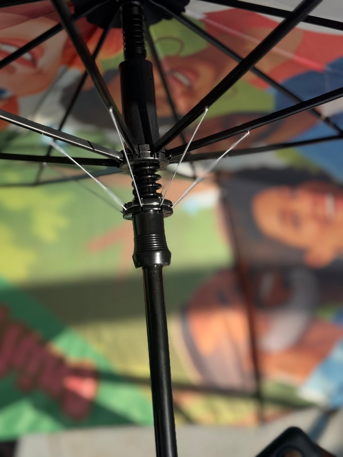 Close-up of an umbrella's black shaft and metal spokes against a colorful background